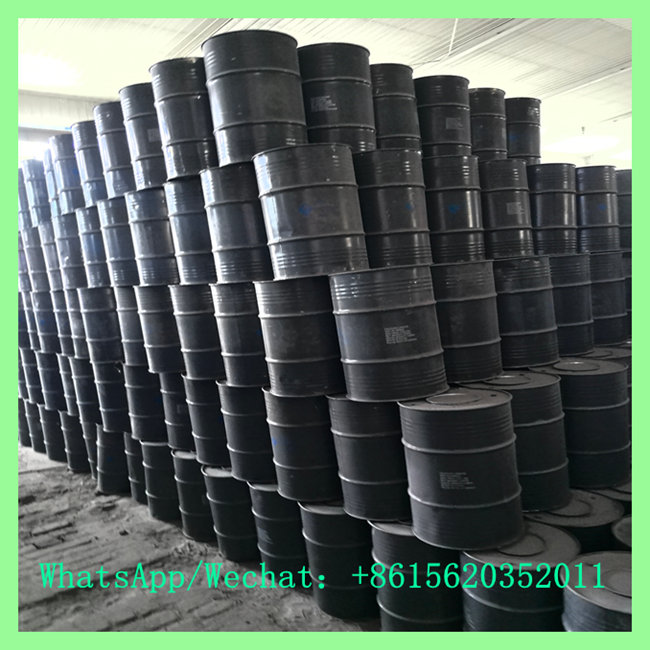 A large stack of black metal chemical drums filled high inside a industrial storage facility.