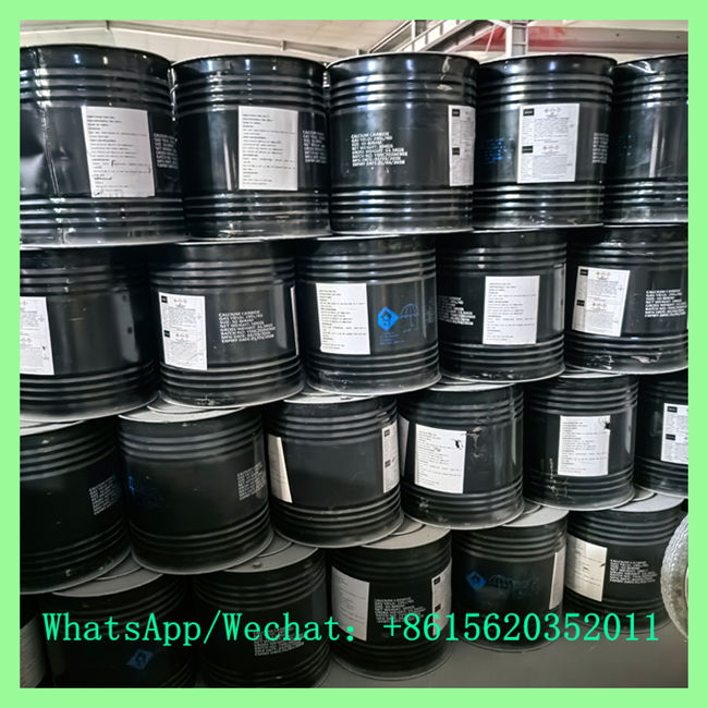 Black industrial steel drums neatly stacked with white product specification labels and blue GHS hazard placards.