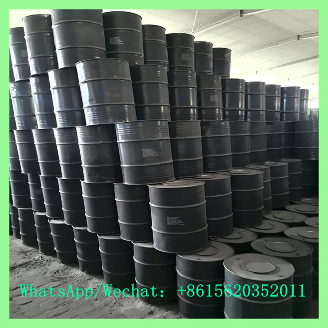 A massive pile of black metal chemical drums stacked high inside an industrial factory warehouse.