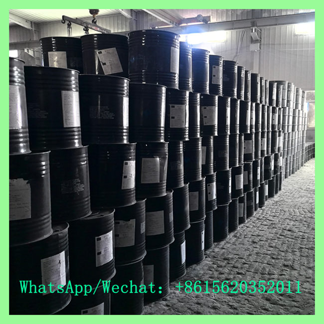 Large-scale storage of black metal chemical drums stacked in tall rows stretching down a factory warehouse corridor.