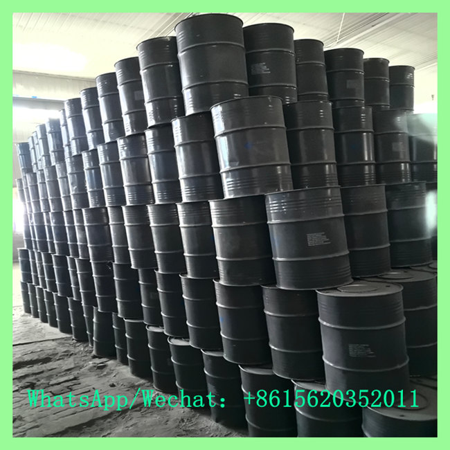 High stack of black steel drums organized in tall, dense rows along a industrial concrete floor.