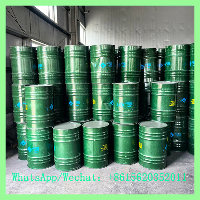 Green industrial steel drums stacked vertically in a warehouse, featuring blue hazard placards and product identification text.