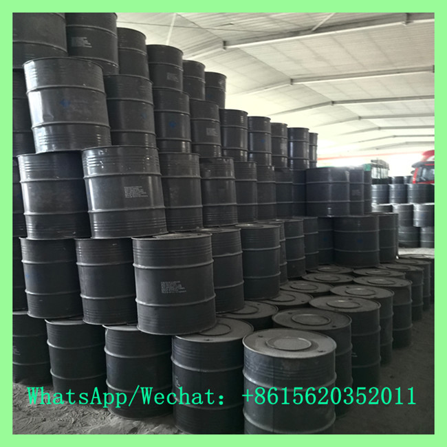 A massive array of black metal chemical drums stacked high inside a spacious manufacturing warehouse.