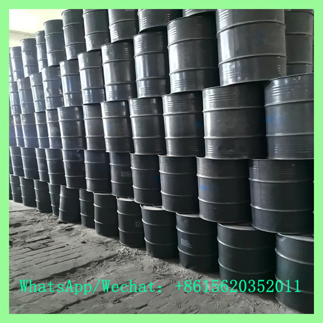 Black metal industrial drums stacked in high tiers on a concrete floor inside a large industrial factory building