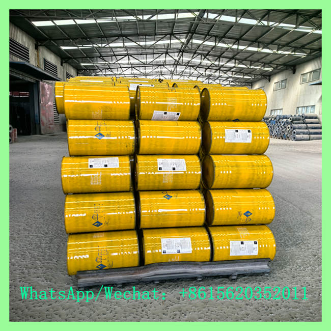 Bright yellow industrial metal drums horizontally stacked on a pallet inside a warehouse, featuring product specification labels and hazard warning symbols.