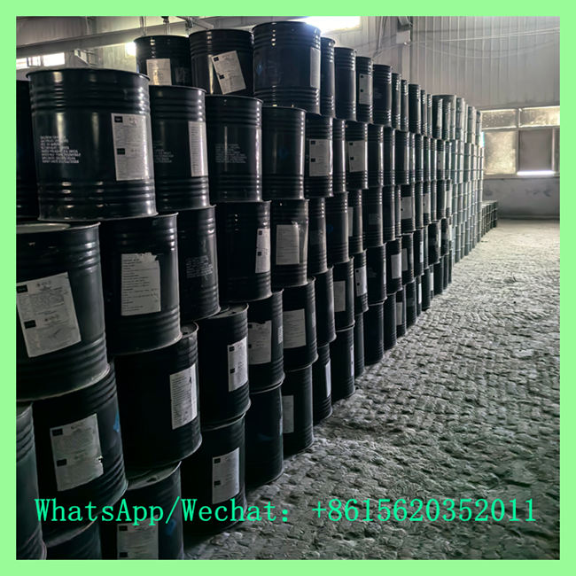 Perspective view of black chemical drums stacked neatly in long, tall rows along a factory warehouse floor.