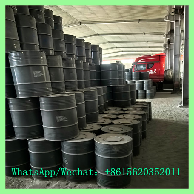 Large stock of steel drums stacked high in a warehouse loading area, with a red transport truck parked in the background.