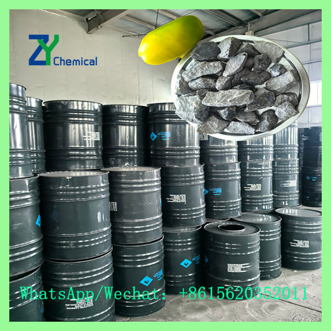 Close-up of grey calcium carbide lumps next to stacked export steel drums for sale near me